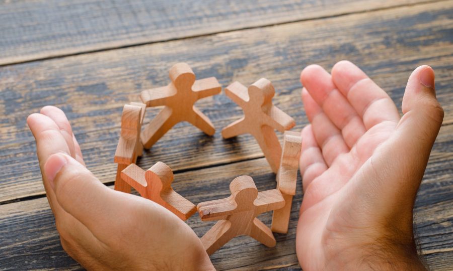 Business success concept on wooden background high angle view. hands protecting wooden figures of people.